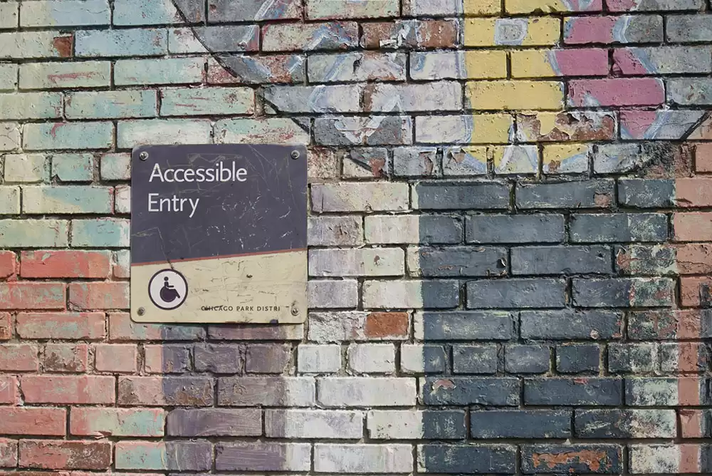 A standard ADA sign on a brick wall that says Accessible Entry