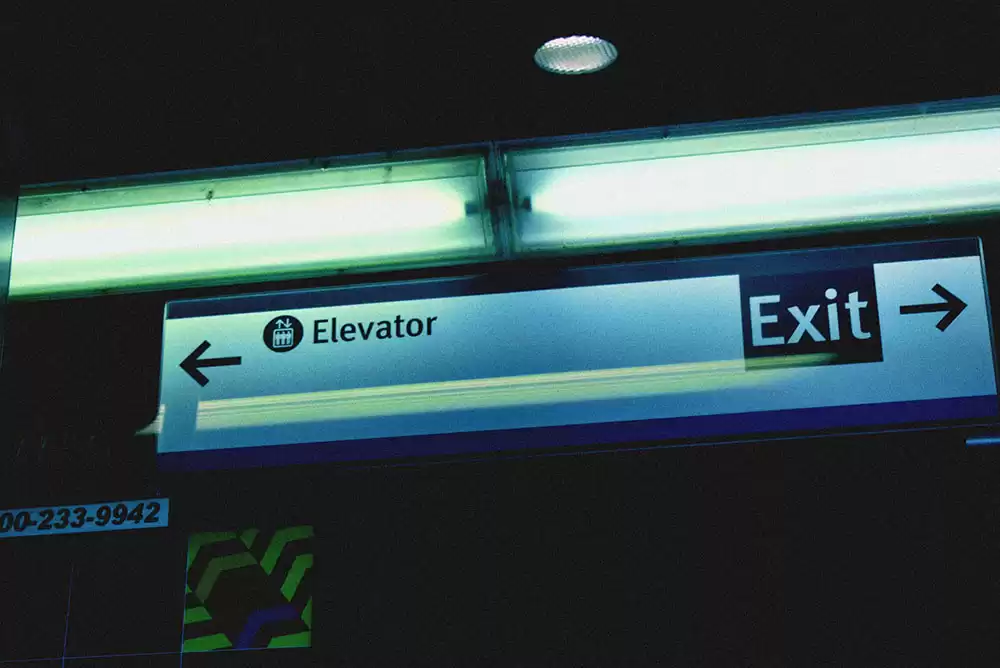 An ADA approved sign showing the way to the elevator and exit.